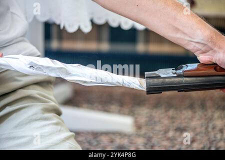 Ein Mann reinigt ein altes Gewehr sorgfältig mit Öl und Reinigungsgeräten und zeigt die Liebe zum Detail und die Handwerkskunst alter Schusswaffen. Stockfoto