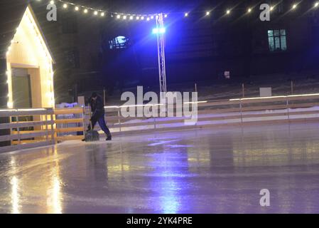 Weihnachtsstimmung zu Silvester. Ein Mann in Arbeitskleidung sammelt Eis an einer Eislaufbahn mit Beleuchtung im Zentrum der Stadt Dnipro, Dnipropetrowsk, Stockfoto