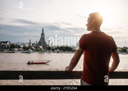 Rückansicht des Menschen vor dem Stadtbild mit Chao Phraya River und Wat Arun bei Sonnenuntergang. Reisende genießen eine wunderschöne Aussicht auf Bangkok, Thailand. Stockfoto