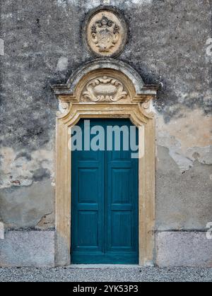 Italienisches altes Dorf, Castellaro Lagusello in der Nähe von Mantua. Eine dekorative türkisfarbene Tür aus dem 18. Jahrhundert steht vor einer verwitterten Steinmauer. Stockfoto