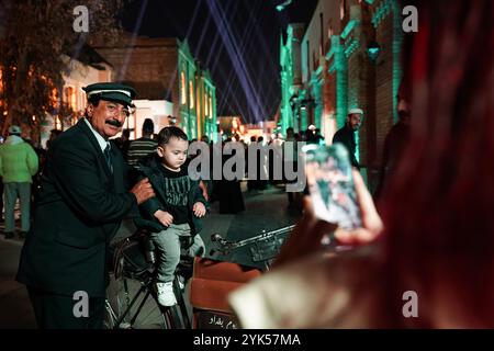 Bagdad, Irak. November 2024. Eine junge Frau fotografiert ein Kind, das mit einem Mann sitzt, der als Postbote gekleidet ist und mit seinem Fahrrad beim Bagdad Day Festival in der Al-Saray Street steht. Das Bagdad Day Festival feiert die Geschichte und Zivilisation Bagdads. Die Veranstaltung „Bagdad Simulation“, eines der Segmente des Festivals, das die Atmosphäre der Stadt in einer Zeit von 1924 bis 2024 wiederbeleben soll, indem traditionelle Charaktere und wesentliche Rollen neu verkörpert werden, die eine zentrale Rolle im täglichen Leben in Bagdad spielten. (Credit Image: © Ismael Adnan/SOPA Images via ZUMA Press Wire) ED Stockfoto