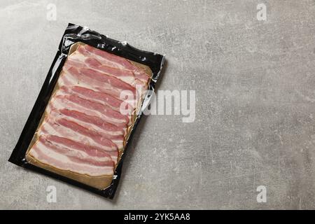 Packung mit geschnittenem Speck auf grauem Tisch, Draufsicht. Leerzeichen für Text Stockfoto