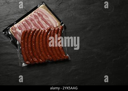 Packungen Würstchen und Speck auf schwarzem Tisch, Draufsicht. Leerzeichen für Text Stockfoto