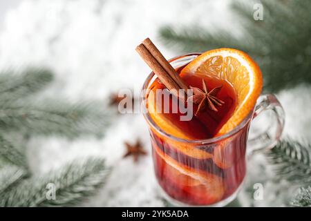 Glühwein in Glasgläsern, dekoriert mit Zimtstangen auf schneebedeckten Holztisch, in der Nähe sind grüne Fichtenzweige. Weihnachtsgetränk, Silvester-Punsch. Stockfoto