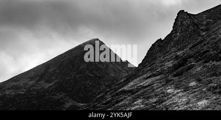 Eine beeindruckende Berglandschaft mit scharfen Gipfeln und felsigen Hängen unter bewölktem Himmel. Der Schwarz-weiß-Kontrast unterstreicht das raue Gelände, EM Stockfoto