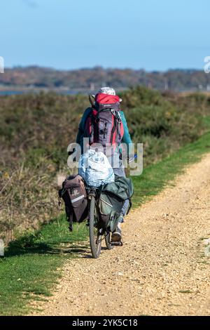 Mann, der mit schwer beladenen Koffer unterwegs ist, fährt auf einer unbefestigten Landstraße oder einem unbefestigten Pfad Stockfoto