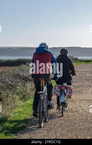 Zwei Radfahrer mittleren Alters in kaltem Wetter, die auf einem öffentlichen Fußweg oder Radweg fahren, ein älteres Paar auf einer gemeinsamen Radtour auf der Landstraße. Stockfoto