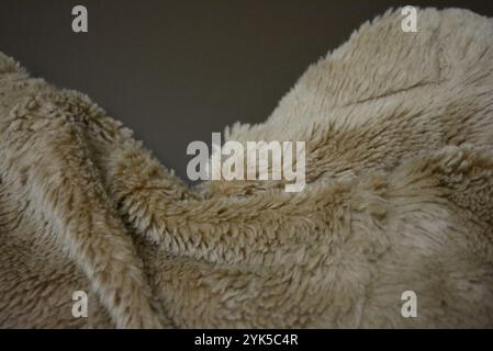Eine flauschige beige Decke ist auf einem matten braunen Hintergrund gesetzt. Der Stoff besteht aus Wolle mit langem Stapel und Überzug. Stockfoto