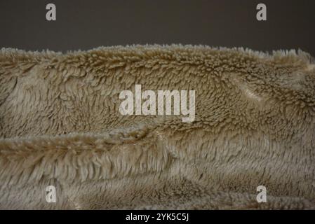 Eine flauschige beige Decke ist auf einem matten braunen Hintergrund gesetzt. Der Stoff besteht aus Wolle mit langem Stapel und Überzug. Stockfoto
