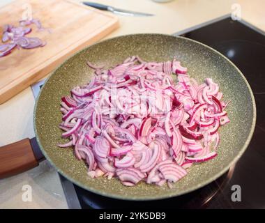 Rote Zwiebeln werden in dünne Scheiben geschnitten und ordentlich in einer Pfanne angeordnet, fertig zum Kochen in einer modernen Küche. Stockfoto