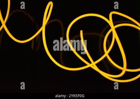 Schöne dicke gelbe, orangefarbene Drähte sind chaotisch angeordnet und auf einem schwarzen Kunststoffhintergrund verdreht. Elektrolumineszenzkabel, Neonröhren. Stockfoto