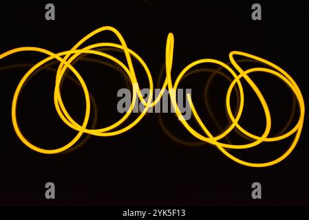 Schöne dicke gelbe, orangefarbene Drähte sind chaotisch angeordnet und auf einem schwarzen Kunststoffhintergrund verdreht. Elektrolumineszenzkabel, Neonröhren. Stockfoto