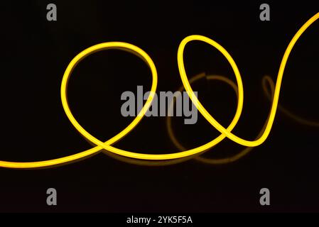 Schöne dicke gelbe, orangefarbene Drähte sind chaotisch angeordnet und auf einem schwarzen Kunststoffhintergrund verdreht. Elektrolumineszenzkabel, Neonröhren. Stockfoto