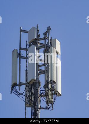 Eine Nahaufnahme eines Mobilfunkturms mit Antennen vor einem hellblauen Himmel Stockfoto