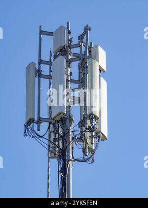 Ein hoher Mobilfunkturm mit mehreren Antennen vor einem klaren blauen Himmel Stockfoto