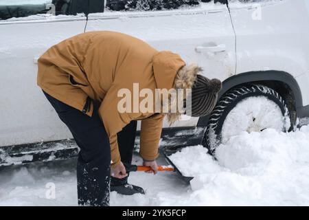 Ein Mann gräbt mit einer Schaufel ein festgefahrene Auto im Schnee aus. Der Transport im Winter ist in der Schneeverwehung nach dem Schneefall stecken geblieben, saß auf dem Boden. Zuerst ai Stockfoto