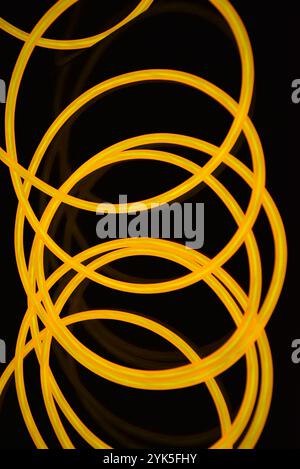 Schöne dicke gelbe, orangefarbene Drähte sind chaotisch angeordnet und auf einem schwarzen Kunststoffhintergrund verdreht. Elektrolumineszenzkabel, Neonröhren. Stockfoto
