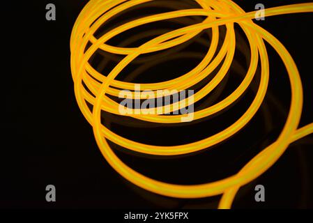 Schöne dicke gelbe, orangefarbene Drähte sind chaotisch angeordnet und auf einem schwarzen Kunststoffhintergrund verdreht. Elektrolumineszenzkabel, Neonröhren. Stockfoto