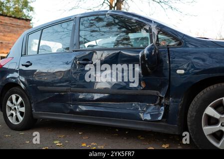 Beschädigtes blaues Auto mit Dellen und Kratzern an der Seite, die die Folgen eines Unfalls oder einer Kollision in einer städtischen Umgebung im Freien zeigen. Stockfoto