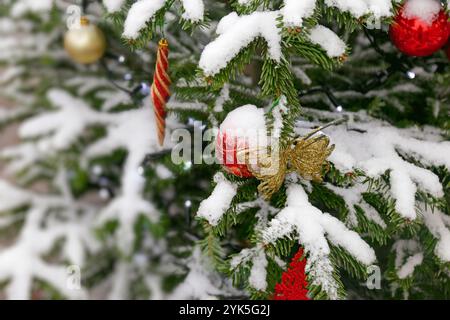 Der Weihnachtsbaum ist mit Schnee bedeckt und hat viele andere Ornamente. Prächtiger farbenfroher Weihnachtsbaum im Freien Stockfoto