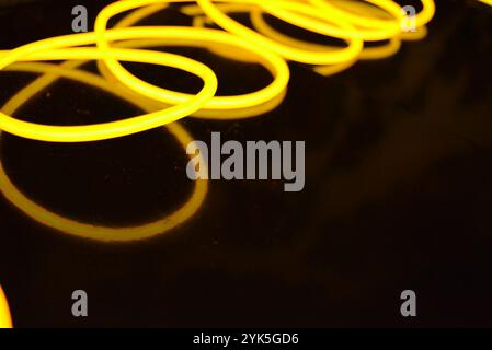Schöne dicke gelbe, orangefarbene Drähte sind chaotisch angeordnet und auf einem schwarzen Kunststoffhintergrund verdreht. Elektrolumineszenzkabel, Neonröhren. Stockfoto