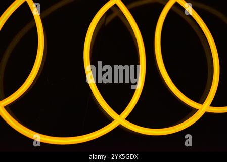 Schöne dicke gelbe, orangefarbene Drähte sind chaotisch angeordnet und auf einem schwarzen Kunststoffhintergrund verdreht. Elektrolumineszenzkabel, Neonröhren. Stockfoto