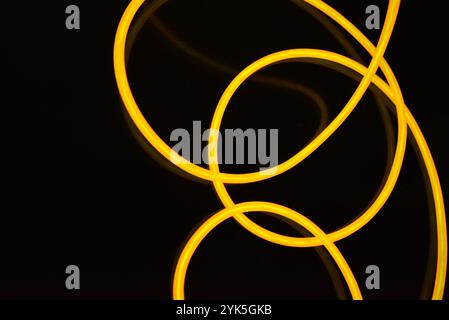 Schöne dicke gelbe, orangefarbene Drähte sind chaotisch angeordnet und auf einem schwarzen Kunststoffhintergrund verdreht. Elektrolumineszenzkabel, Neonröhren. Stockfoto