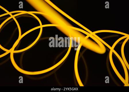 Schöne dicke gelbe, orangefarbene Drähte sind chaotisch angeordnet und auf einem schwarzen Kunststoffhintergrund verdreht. Elektrolumineszenzkabel, Neonröhren. Stockfoto