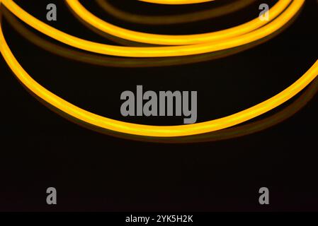 Schöne dicke gelbe, orangefarbene Drähte sind chaotisch angeordnet und auf einem schwarzen Kunststoffhintergrund verdreht. Elektrolumineszenzkabel, Neonröhren. Stockfoto