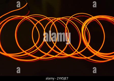 Ungewöhnliches, dünnes rotes Gewinde, verdrillter Draht, strukturelles und gebogenes Kabel. Neon-Elektrolumineszenzkabel, Draht, Kunststoff strahlt Neonlicht gleichmäßig aus. Stockfoto