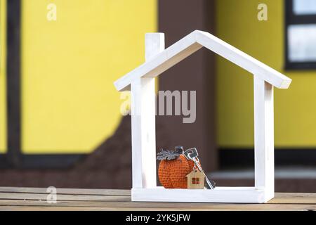 Herbstdekor auf der Veranda des gelben Hauses außerhalb von Kürbis, Laterne, Girlanden und Figur des Hauses und Schlüssel. Halloween-Party, Herbststimmung, Erntefest Stockfoto
