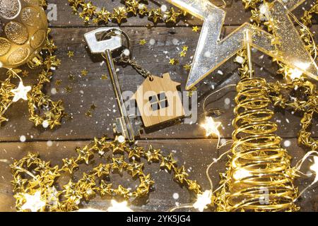 Hausschlüssel mit Schlüsselanhänger Hütte auf einem festlichen Hintergrund mit Pailletten, Sterne, Lichter von Girlanden. Frohes neues Jahr-Holzbriefe, Grüße, Gruß ca. Stockfoto