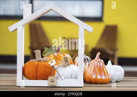 Herbstdekor auf der Veranda des gelben Hauses außerhalb von Kürbis, Laterne, Girlanden und Figur des Hauses und Schlüssel. Halloween-Party, Herbststimmung, Erntefest Stockfoto