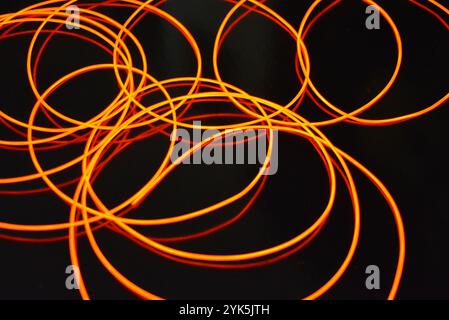 Ungewöhnliches, dünnes rotes Gewinde, verdrillter Draht, strukturelles und gebogenes Kabel. Neon-Elektrolumineszenzkabel, Draht, Kunststoff strahlt Neonlicht gleichmäßig aus. Stockfoto