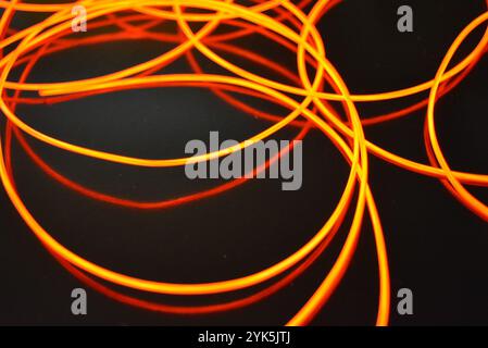 Ungewöhnliches, dünnes rotes Gewinde, verdrillter Draht, strukturelles und gebogenes Kabel. Neon-Elektrolumineszenzkabel, Draht, Kunststoff strahlt Neonlicht gleichmäßig aus. Stockfoto