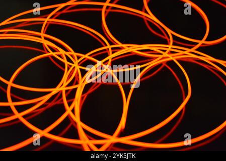 Ungewöhnliches, dünnes rotes Gewinde, verdrillter Draht, strukturelles und gebogenes Kabel. Neon-Elektrolumineszenzkabel, Draht, Kunststoff strahlt Neonlicht gleichmäßig aus. Stockfoto
