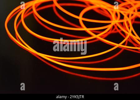 Ungewöhnliches, dünnes rotes Gewinde, verdrillter Draht, strukturelles und gebogenes Kabel. Neon-Elektrolumineszenzkabel, Draht, Kunststoff strahlt Neonlicht gleichmäßig aus. Stockfoto