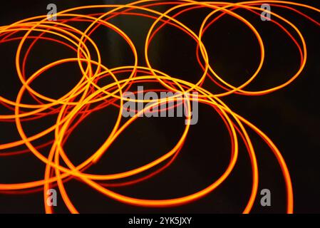 Ungewöhnliches, dünnes rotes Gewinde, verdrillter Draht, strukturelles und gebogenes Kabel. Neon-Elektrolumineszenzkabel, Draht, Kunststoff strahlt Neonlicht gleichmäßig aus. Stockfoto