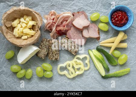 Kalte Vorspeise. Aufschnitt. Verschiedene Snacks auf weißem zerknittertem Papier, Speck, Obst, Trauben, Gemüse, von oben Stockfoto
