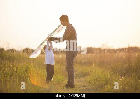 Papa hilft seiner Tochter, im Sommer bei Sonnenuntergang einen Drachen auf einem Feld zu fliegen. Familienunterhaltung im Freien, Vatertag, Kindertag. Ländliche Gebiete, zusatzbereich Stockfoto