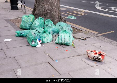 Grüne Müllsäcke in einem Stapel an der High Road in Chiswick warten auf die Abholung mit einer gebrauchten KFC-Verpackung in der Nähe von London. Konzept: Abfall, Abfallsammlung Stockfoto