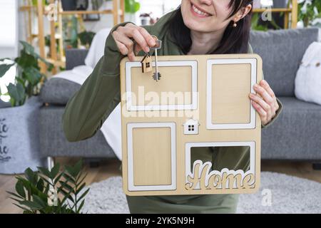 Happy Woman in House hält einen Bilderrahmen mit Figur zu Hause Vorlage und Schlüssel im Innenraum in den Händen. Traumhausprojekt, Immobilienkauf, Versicherung Stockfoto