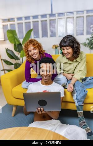 Vertikales Foto von drei multirassischen LGTB-Menschen, die zusammen auf einem modernen Sofa sitzen Stockfoto