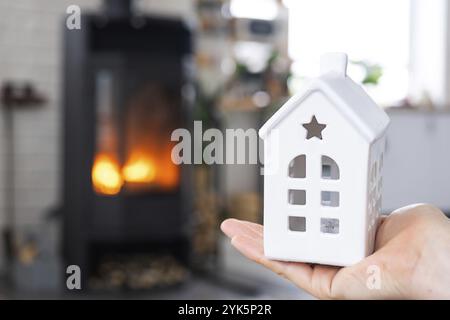 Schlüssel zum Haus mit Schlüsselanhänger in der Hand Besitzer gegen Kamin Herd mit Feuer und Brennholz. Gemütliches Heim. Gebäude, Design, Projekt, Umstieg auf neues Stockfoto