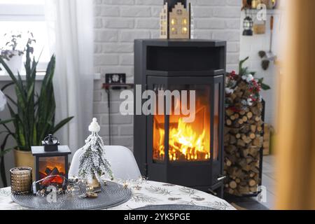 Schwarzer Metallofen, brennender Kamin im weißen festlichen Inneren des Hauses ist für Weihnachten und Neujahr dekoriert, Weihnachtsbaum. Brennholz in t Stockfoto