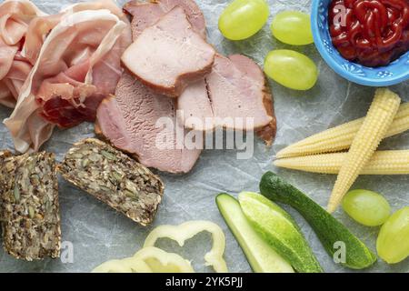Kalte Vorspeise. Aufschnitt. Verschiedene Snacks auf weißem zerknittertem Papier, Speck, Obst, Trauben, Gemüse, von oben Stockfoto