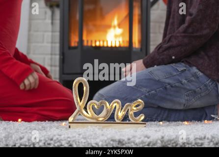 Mann und Frau, die sich zu Hause lieben, sitzen in der Nähe des Kaminherds mit einem brennenden Feuer auf einem gemütlichen Teppich. Valentinstag, glückliches Paar, Liebesgeschichte, Stockfoto