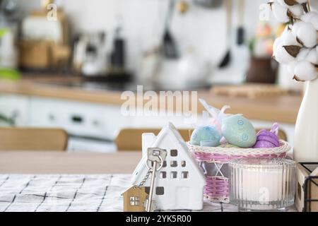 Schlüssel und winziges Haus mit gemütlichem Haus mit Osterdekor mit farbigen Eiern auf dem Tisch der Küche. Bauen, Design, Projekt, Umzug in ein neues Haus, Hypothek, Insur Stockfoto