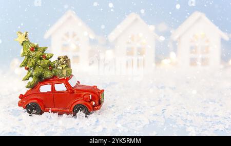 Weihnachtsdekor, rotes Retro-Auto auf Schnee führt vorbei an weißen Häusern mit Lichtergirlanden im Bokeh-Weihnachtsbaum mit Geschenkboxen auf dem Dach. Spielzeug auf blauem bac Stockfoto