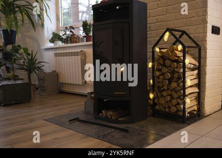 Schwarzer Metallofen Kamin mit Holz in einem Holzhaufen, das Innere eines privaten Dorfhauses. Heizung und Heizung des Hauses mit Brennholz, die Wärme Stockfoto